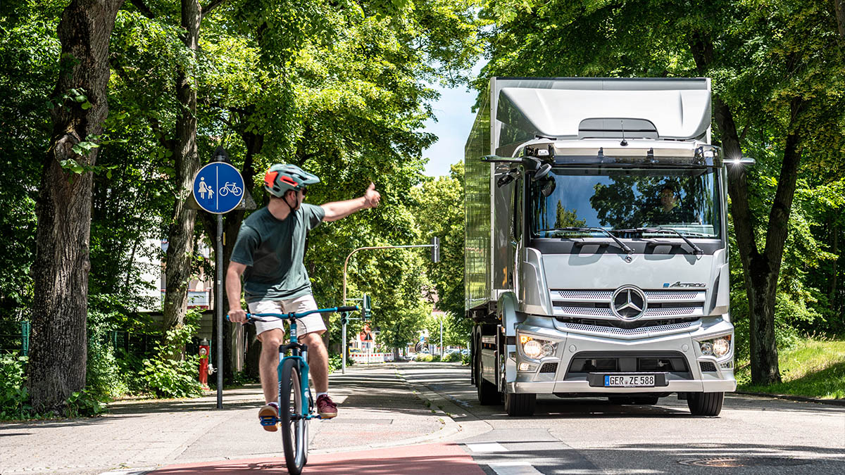 eActros auf Straße mit Fahrradfahrer zur Demonstration der Sicherheit durch Assistenzsysteme bei Autohaus Riess
